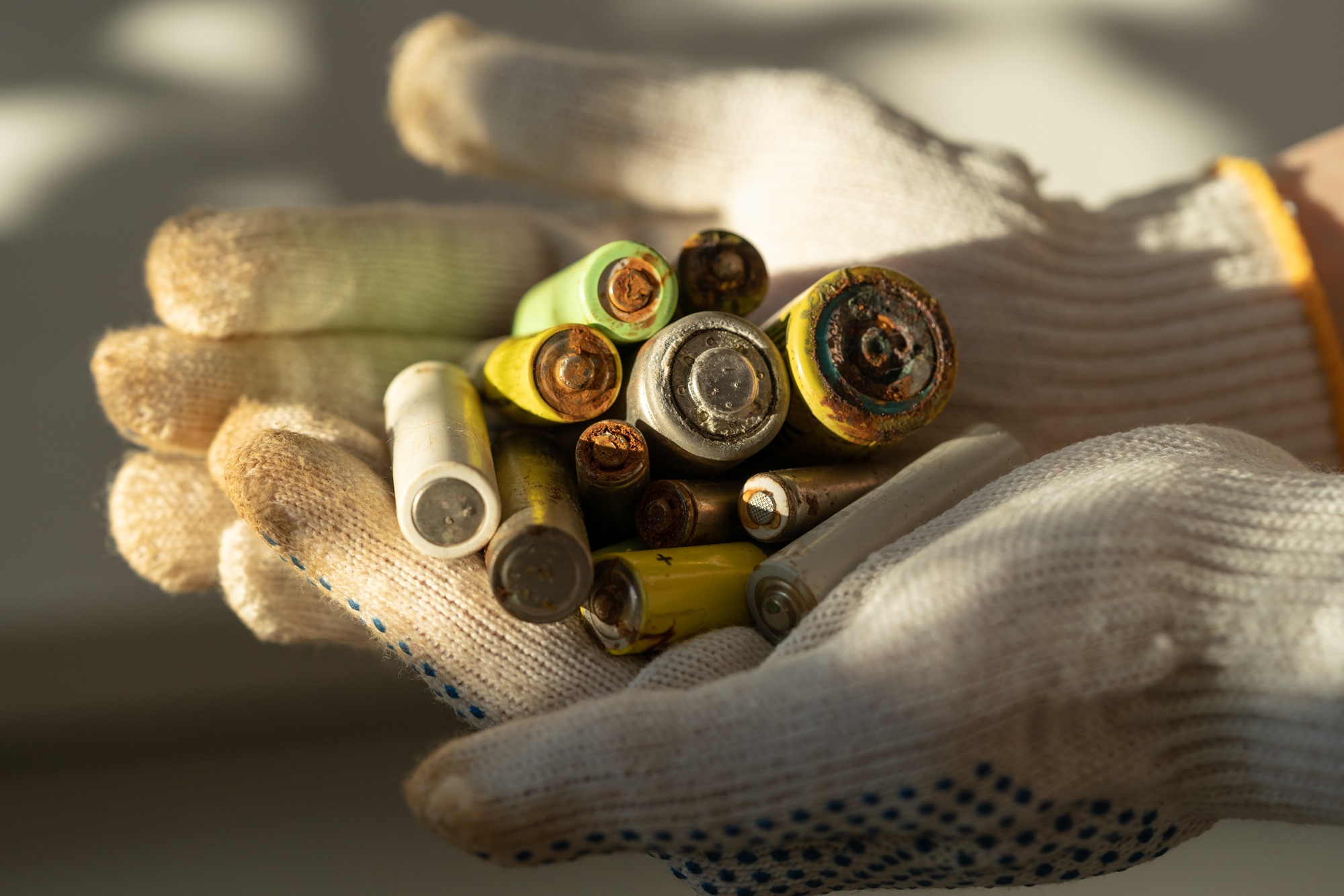 Close up of female hands in cotton protection gloves holding used alkaline batteries heap